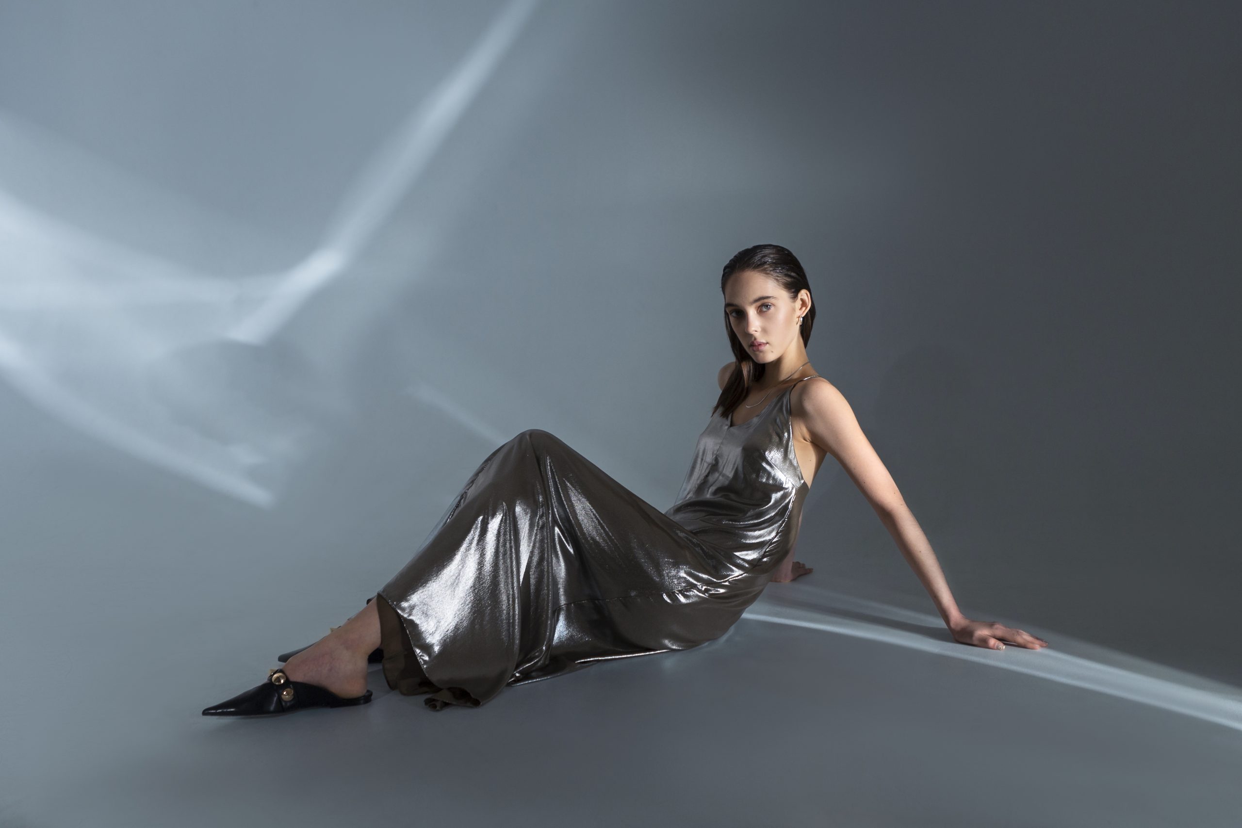 Woman in a metallic silver gown posing on the floor against a gray background.